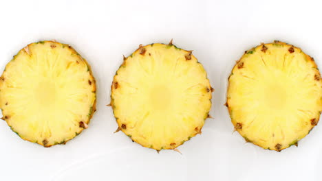 Water-splashes-in-slow-motion.-Top-view:-three-slices-of-sweet-pineapple-washed-with-water-on-a-white-background